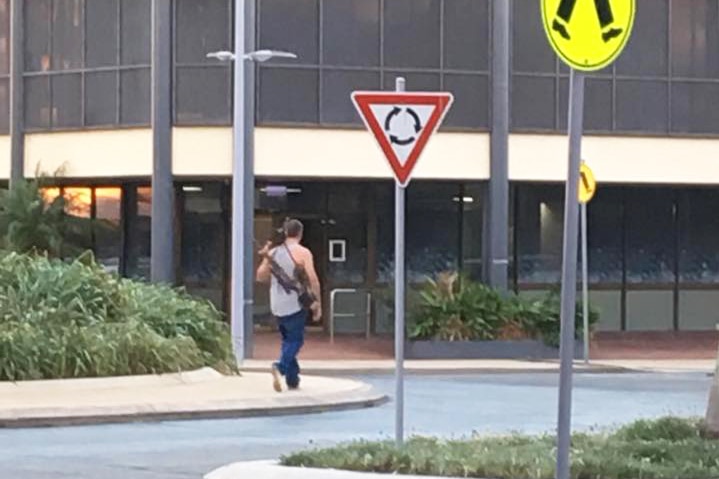 A 29-year-old man carrying two rifles on his back walks down a street in Mackay's CBD in north Queensland.