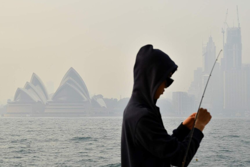 A fisherman in front of the Sydney Opera House surrounded by smoke