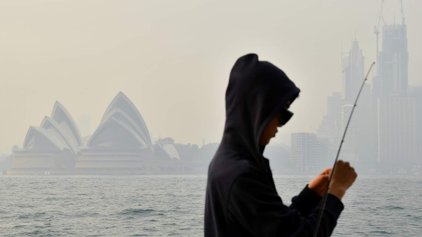 A fisherman in front of the Sydney Opera House surrounded by smoke