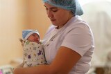A woman in scrubs holds a newborn baby.