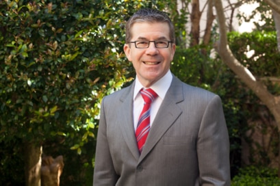 A man wearing a suit and tie smiles.