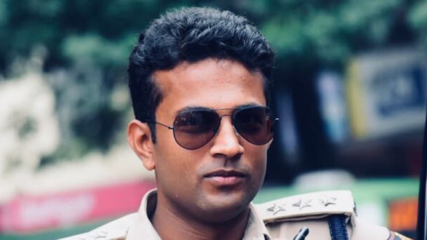 Lokesh Jagalasar looks to the camera. He is wearing aviator glasses and his tan police uniform.
