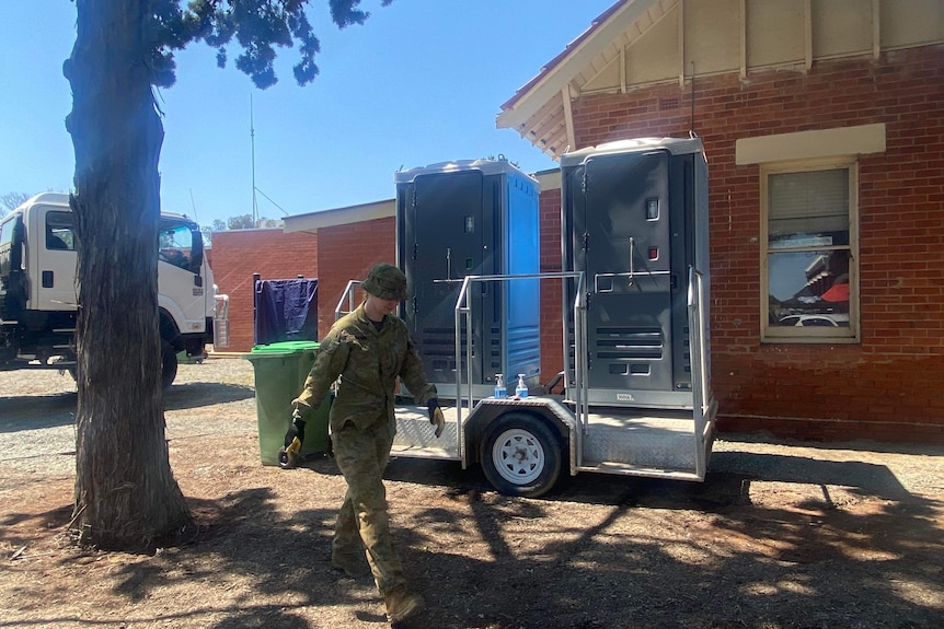 A photo of a soldier walking in front of a portable toilet.