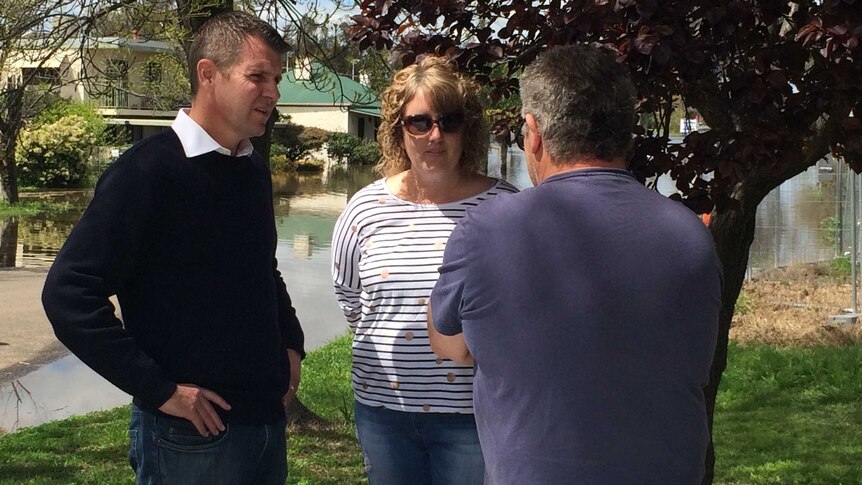 NSW Premier Mike Baird talks with two people, surrounded by floodwaters.