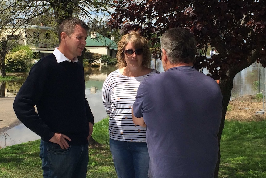 NSW Premier Mike Baird talks with two people, surrounded by floodwaters.