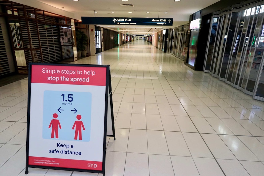 Image of a long empty airport terminal hall with a social distancing sign.