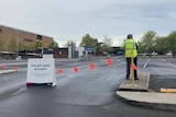 A security guard next to orange bunting at a car park with sign saying "Car park opens at 8:45am"