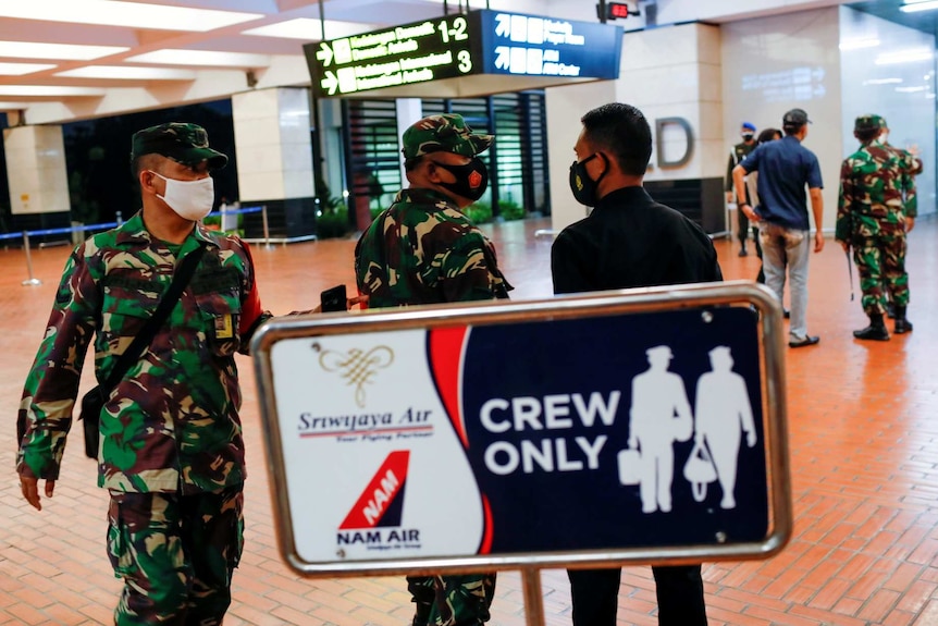 Indonesian soldiers in masks stand at an airport behind a sign reading crew only