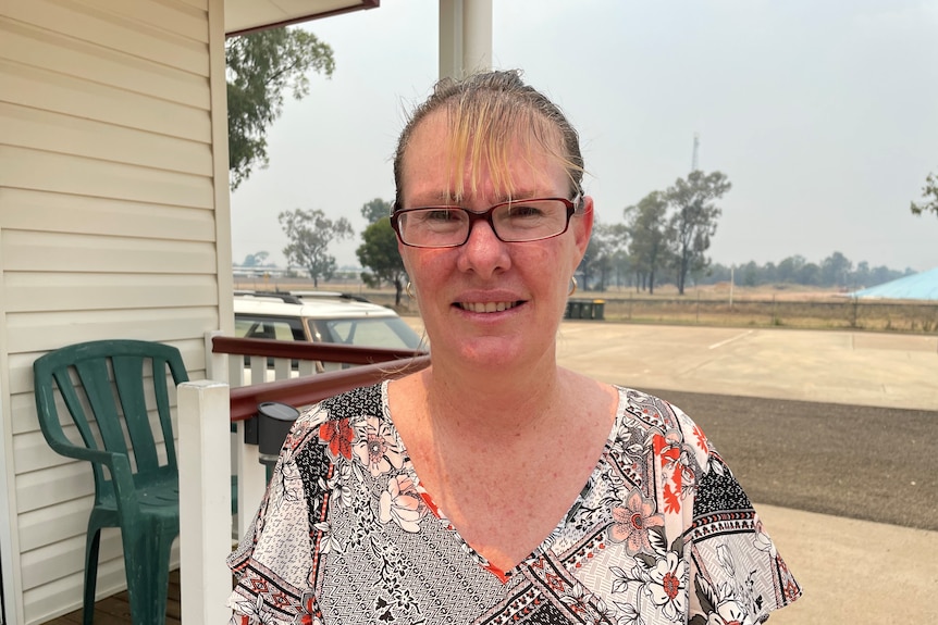 a woman looks directly at the camera and smiles standing outside a small unit at a caravan park