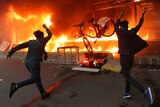 Two protesters hurl a bicycle to a burning metro station with black smoke taking up most of the photo.