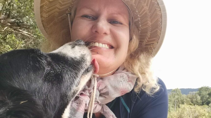 Smiling blonde middle-aged woman in black long-sleeved swimming shirt and straw hat with black and white border collie dog.
