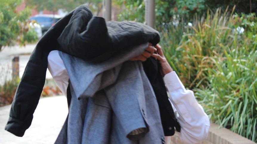 Priyantha Padmike Dayananda covers his head with jackets as he leaves court