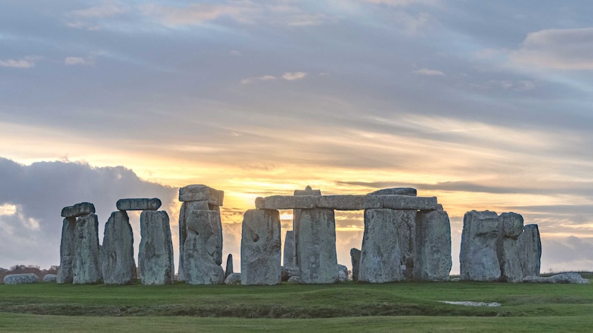 Sun rises through clouds over the stone monument known as Stonehenge.