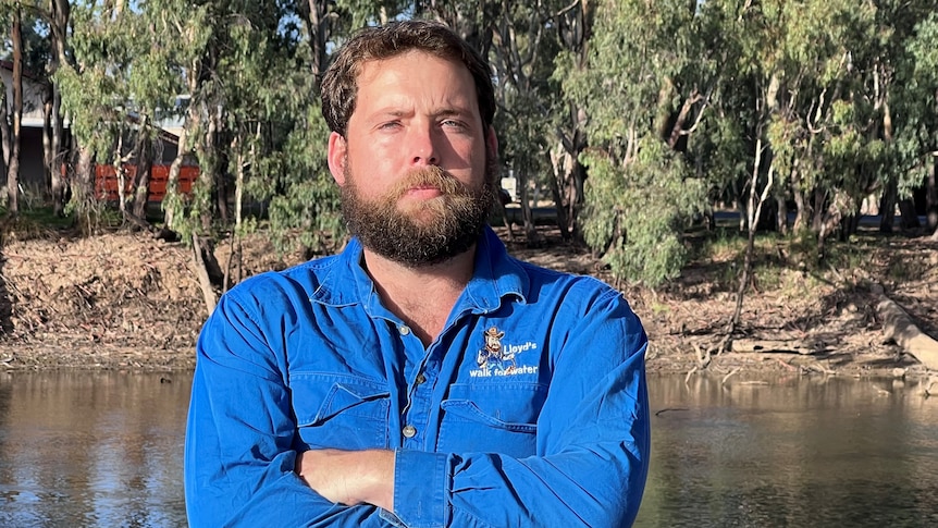 Bearded man in blue work shirt standing on the banks of a river. 