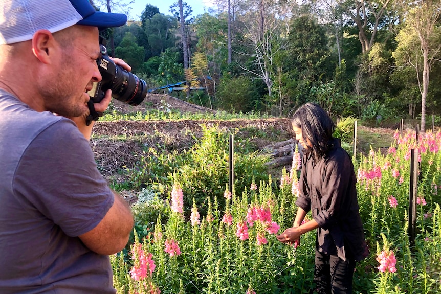A man takes a photo of a woman in a field of flowers.
