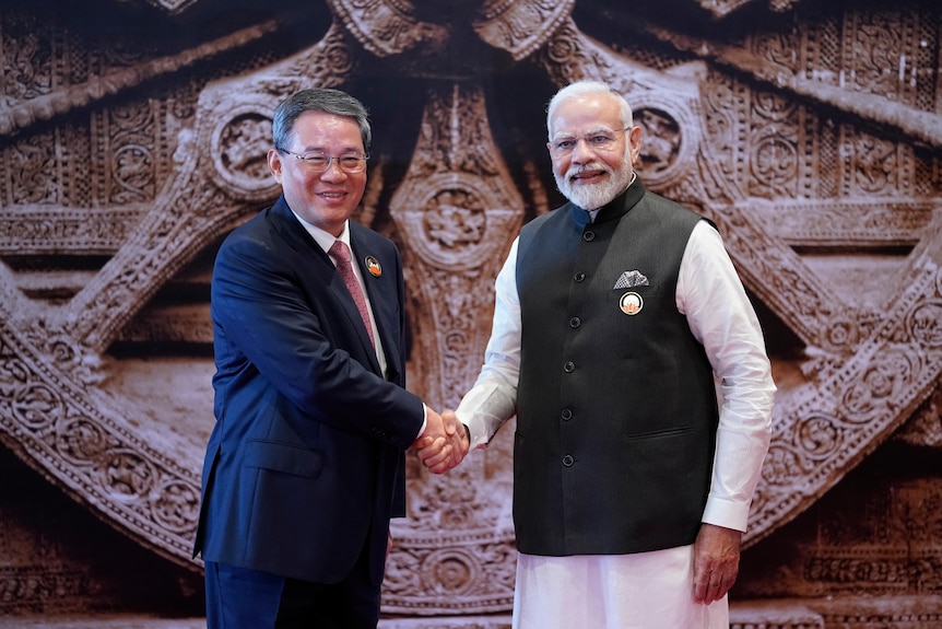 Chinese Premier Li Qiang and Indian Prime Minister Narendra Modi shake hands and smile at the camera