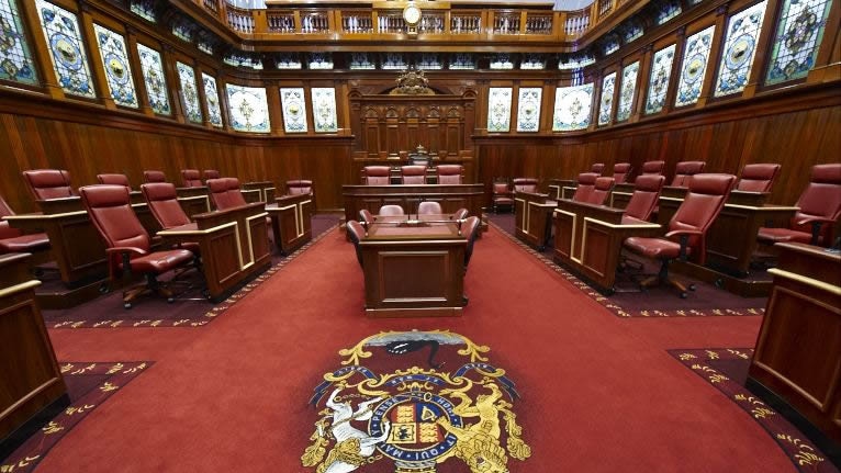 The upper house of WA parliament from inside, showing red carpet and red chairs around a central desk.