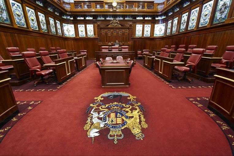 The upper house of WA parliament from inside, showing red carpet and red chairs around a central desk.