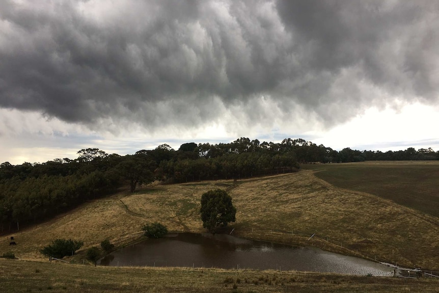 Cloudy skies hang over a dam on a rolling hill.