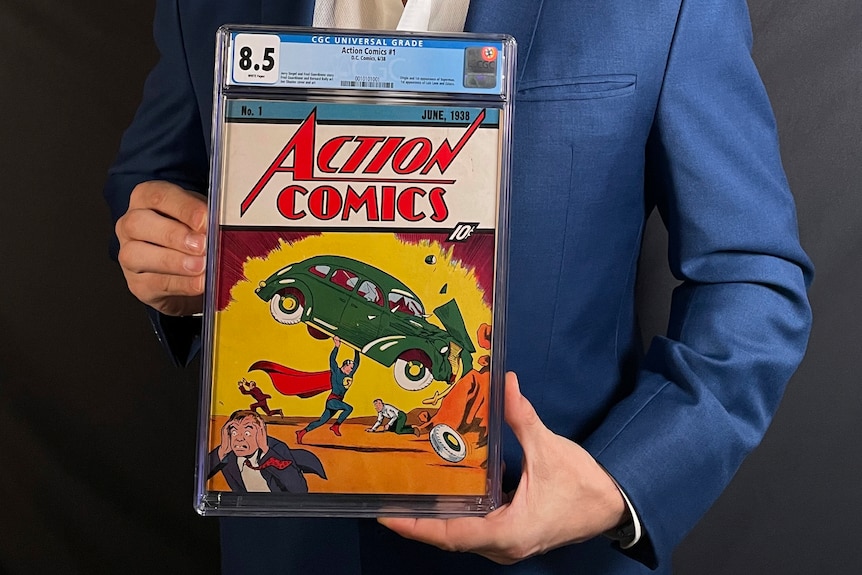 A man holds the comic book. It's cover shows superman holding a car above his head