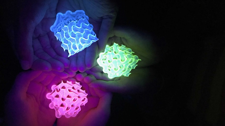 Close-up of three sets of hands holding glowing 3D-printed gyroids.