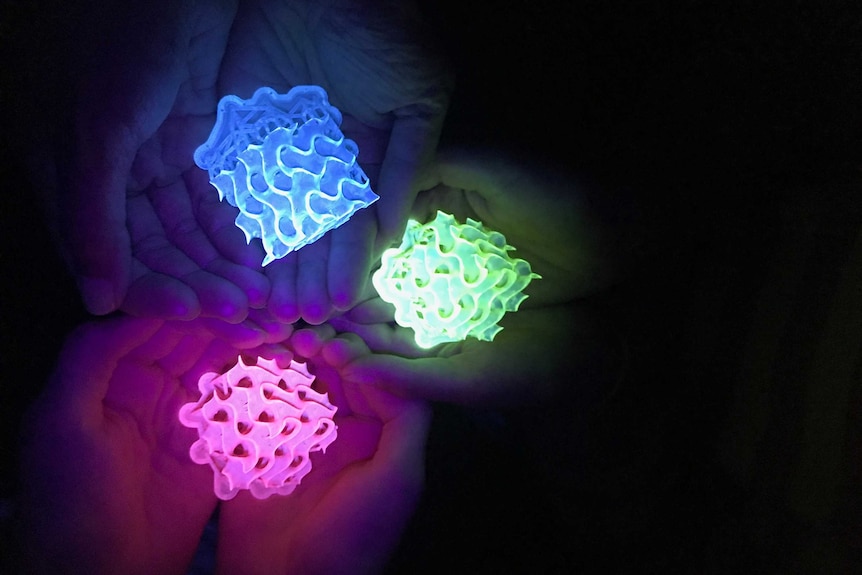 Close-up of three sets of hands holding glowing 3D-printed gyroids.