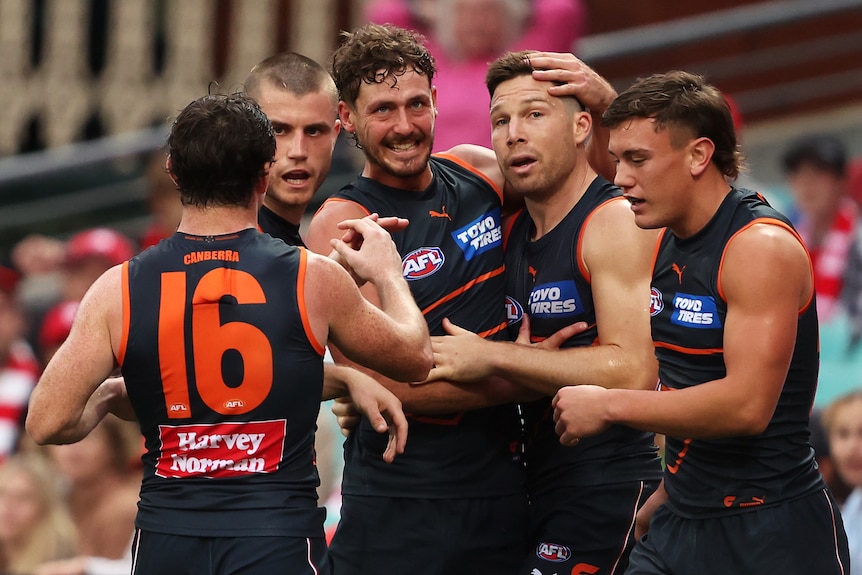 Five GWS Giants AFL players embrace as they celebrate a goal against the Sydney Swans.