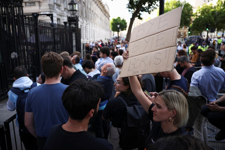 A woman holds a cardboard sign saying "Bye Bye Boris" outside of Downing Street.