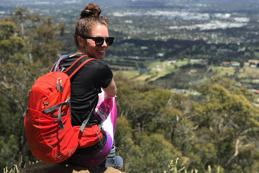 A woman perches on a rock wearing a backpack and hiking boots.