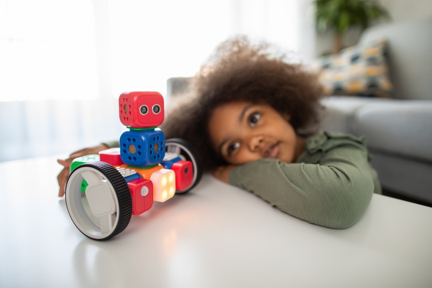 A photo shows a child looking at a colourful robot toy on wheels