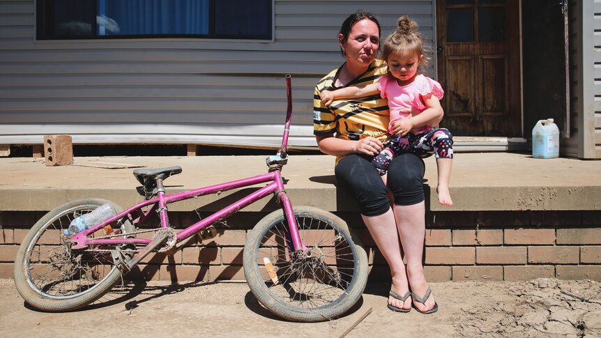A dirty bike, a woman in a football jersey and a small little girl in a pink shirt.