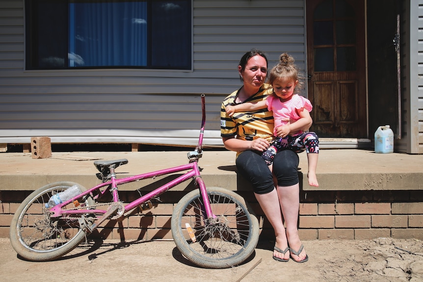 A dirty bike, a woman in a football jersey and a small little girl in a pink shirt.