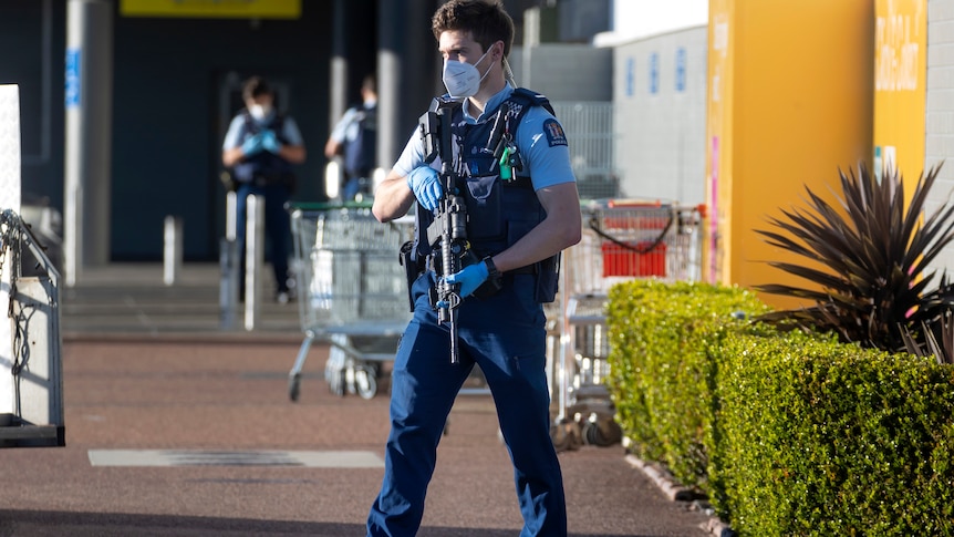 a police officer in uniform holds a rife while walking outside a supermarket in Auckland, New Zealand