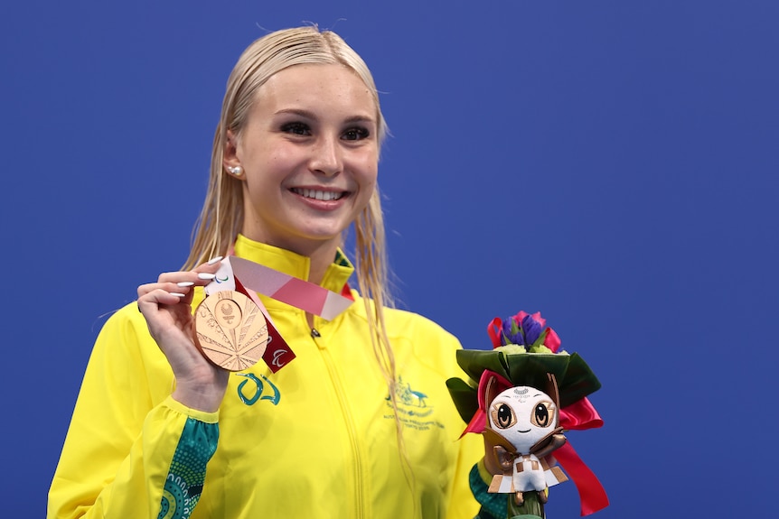 Swimmer stands on the podium with her bronze medal.