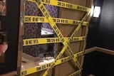 Yellow tape that says crime scene do not cross barricades a hotel room double door, which is missing the left panel