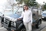 Girl wearing white standing in front of parked small 4WD