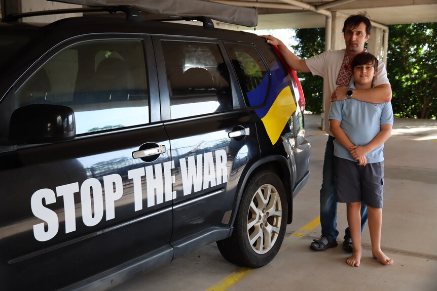A man and his son stand with a car painted with an anti-war slogan.