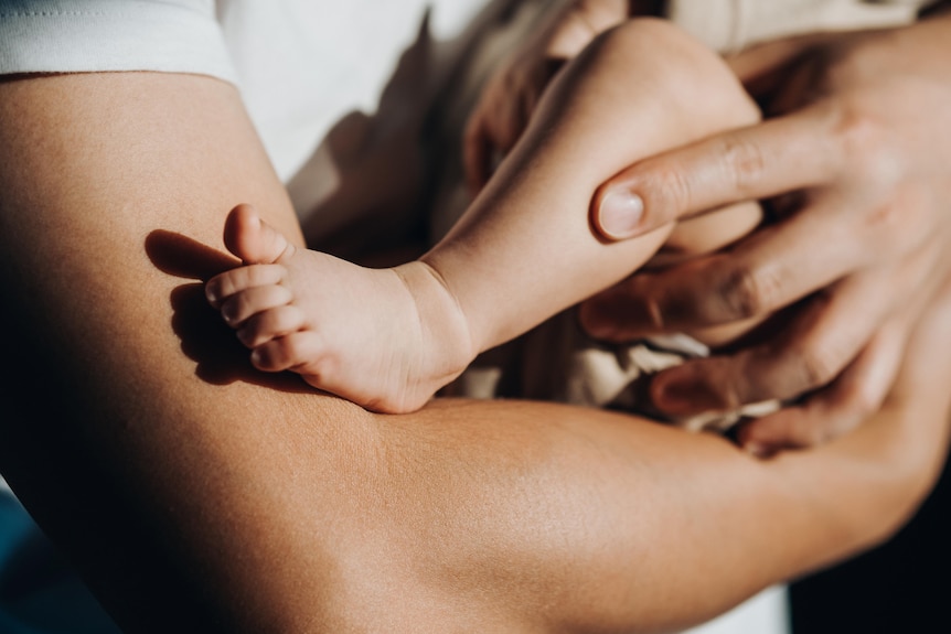 Close up shot of arms holding a small child, whose bare leg and foot are visible.