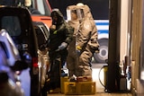 Three people in hazardous material outfits inspect substances on a street in Germany.