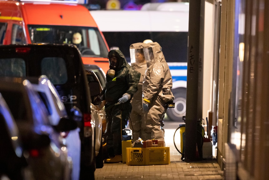 Three people in hazardous material outfits inspect substances on a street in Germany.