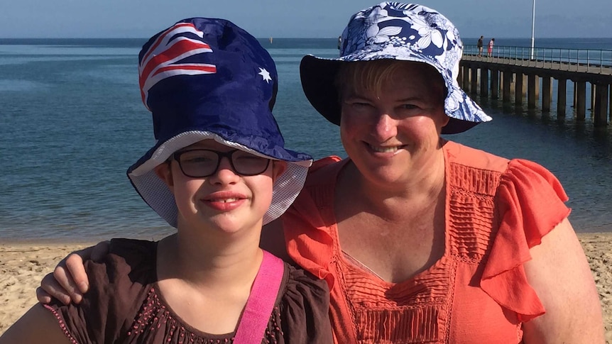 A portrait photo of Rebecca Harvey wearing a novelty Australian flag top hat and her mother Heather Renton standing on a beach.