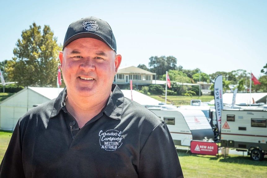 A man wearing a hat and polo shirt stands in front of caravans on display