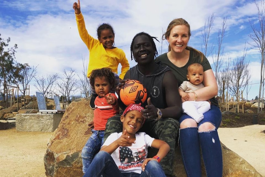 A family of six sitting on a rock in a playground