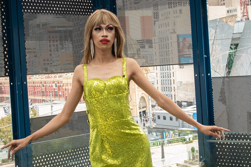 A drag queen wearing a shimmering green gown and a blond wig poses at Federation Square.