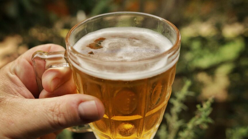 A man's hand holds a beer in a glass.