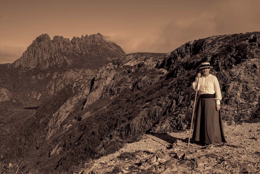 A woman in Edwardian dress on a ridge with the peak of Cradle Mountain behind her.