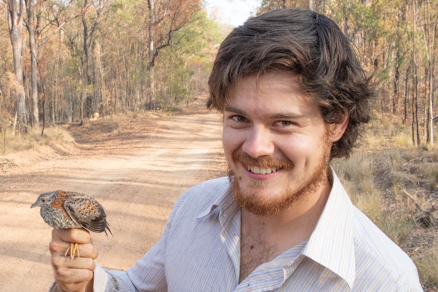 man smile while holding the feet of a bird