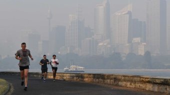 People jog along a running path in front of a smoke-hazed CBD.