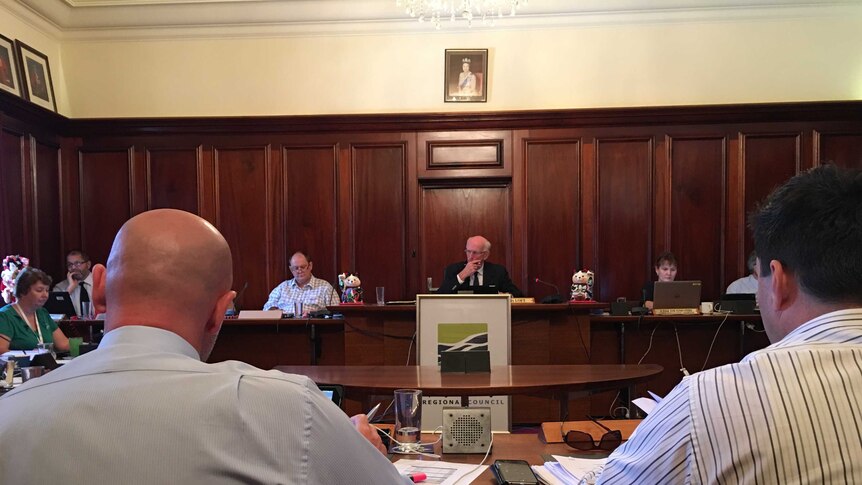 Two men with backs turned to camera read notes in front of desk of fraser coast mayor chris loft and council staff
