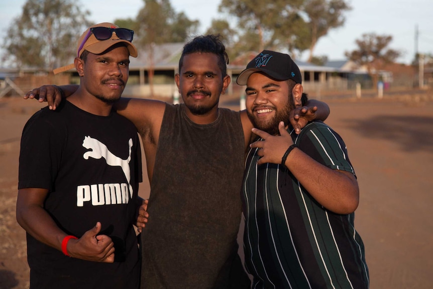 Three young men in embrace inthe street of an outback town.